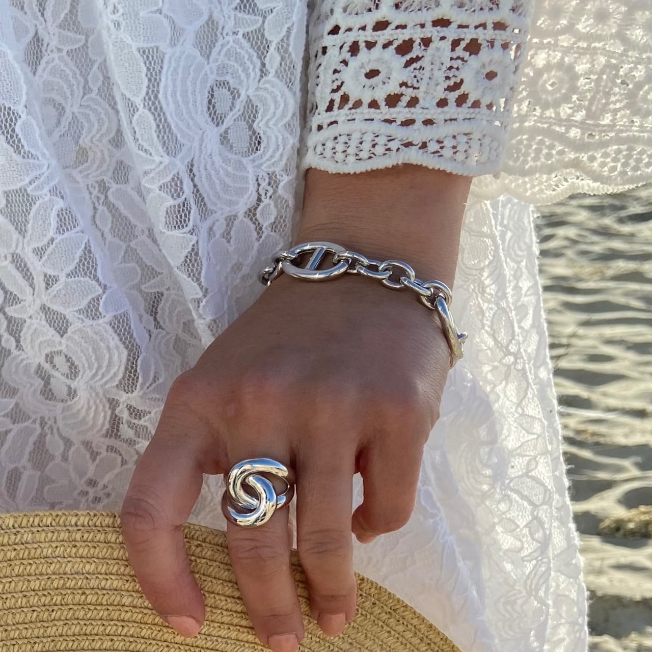 Gros plan sur une main portant une bague et un bracelet argentés, robe dentelle blanche