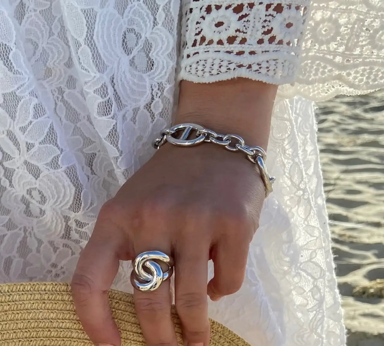 Gros plan sur une main portant une bague et un bracelet argentés, robe dentelle blanche