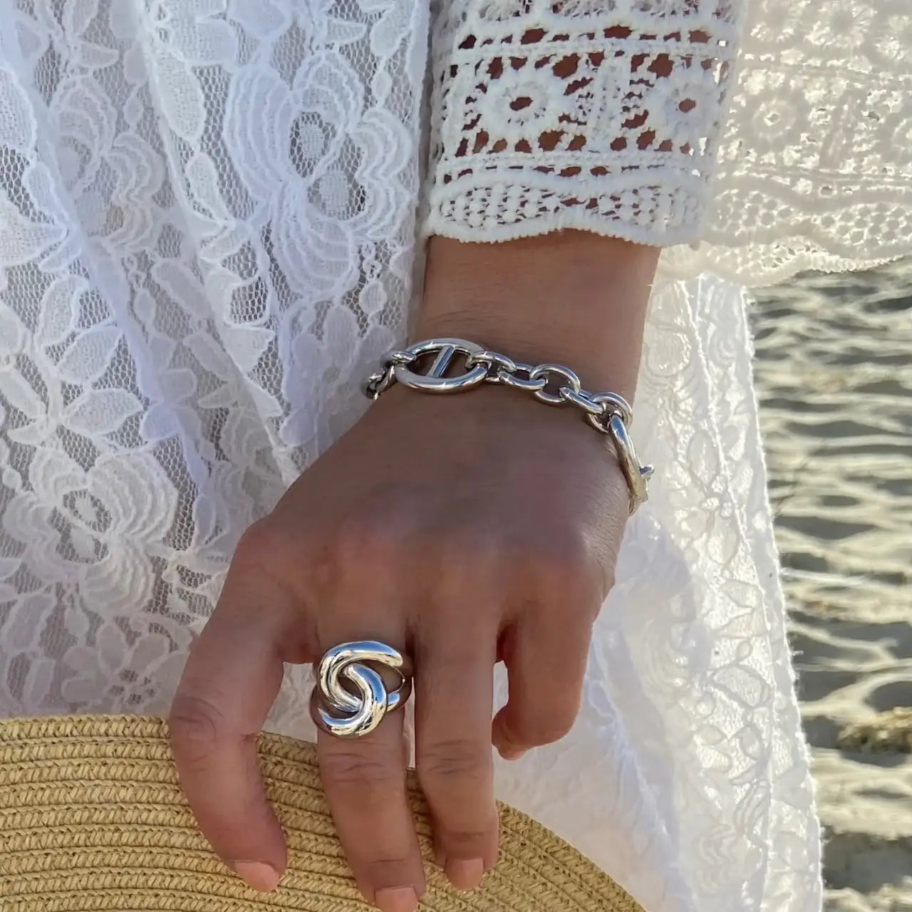 Gros plan sur une main portant une bague et un bracelet argentés, robe dentelle blanche