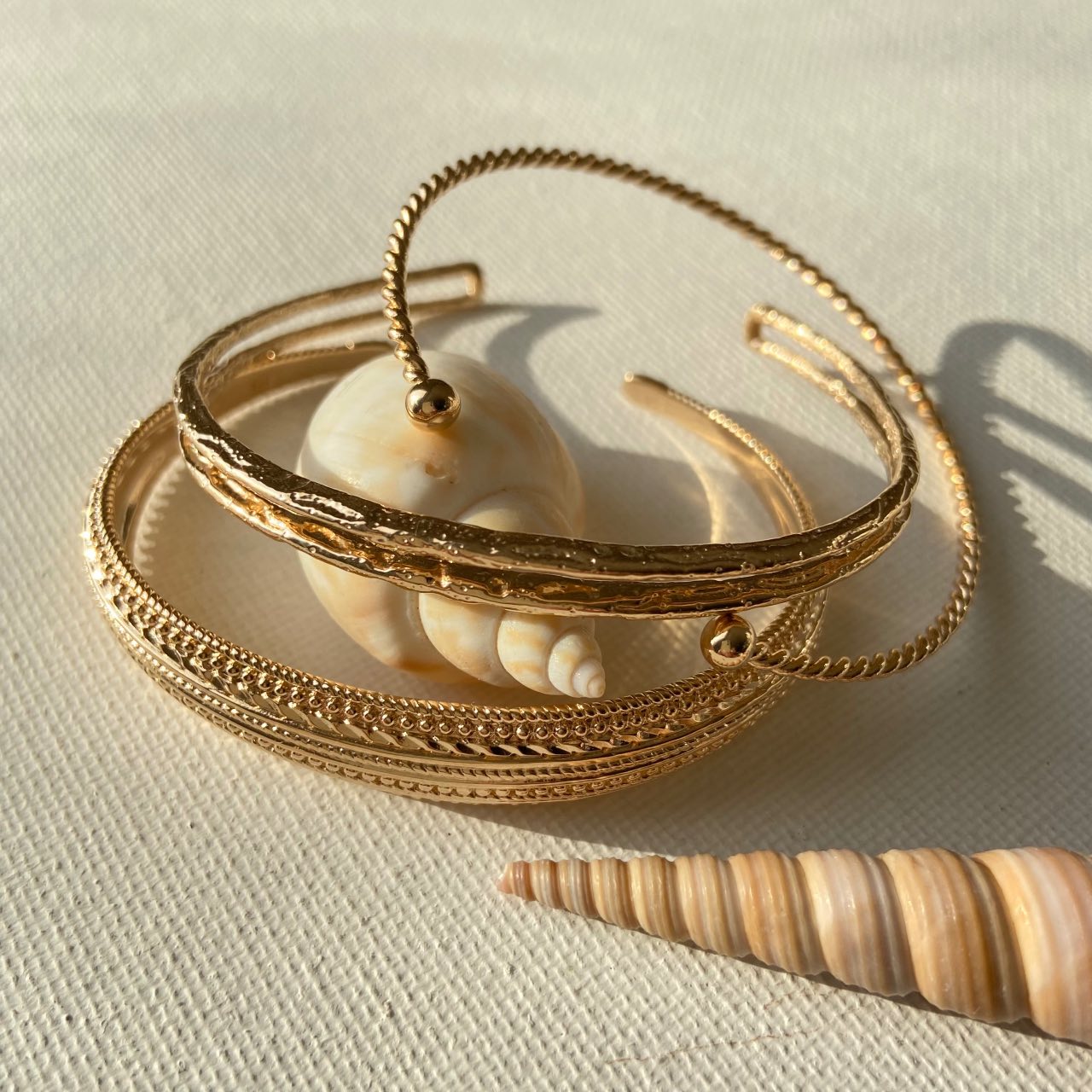 Bracelets ouverts dorés élégants posés près de coquillages sur fond beige, bijoux chic