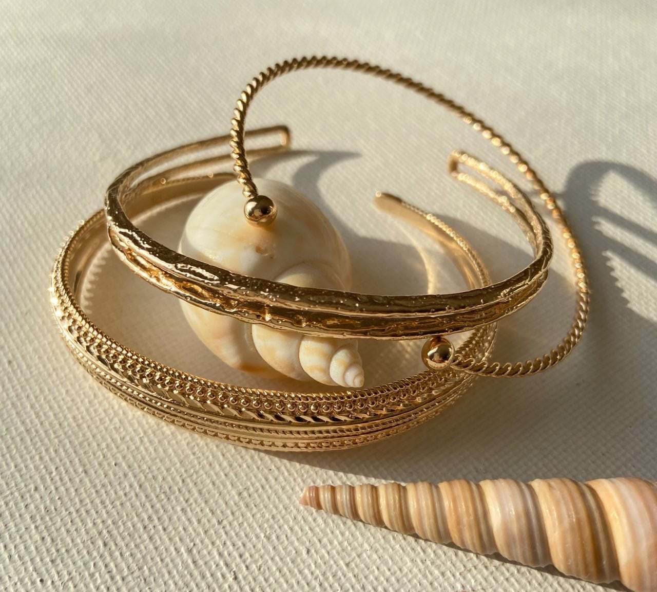 Bracelets ouverts dorés élégants posés près de coquillages sur fond beige, bijoux chic