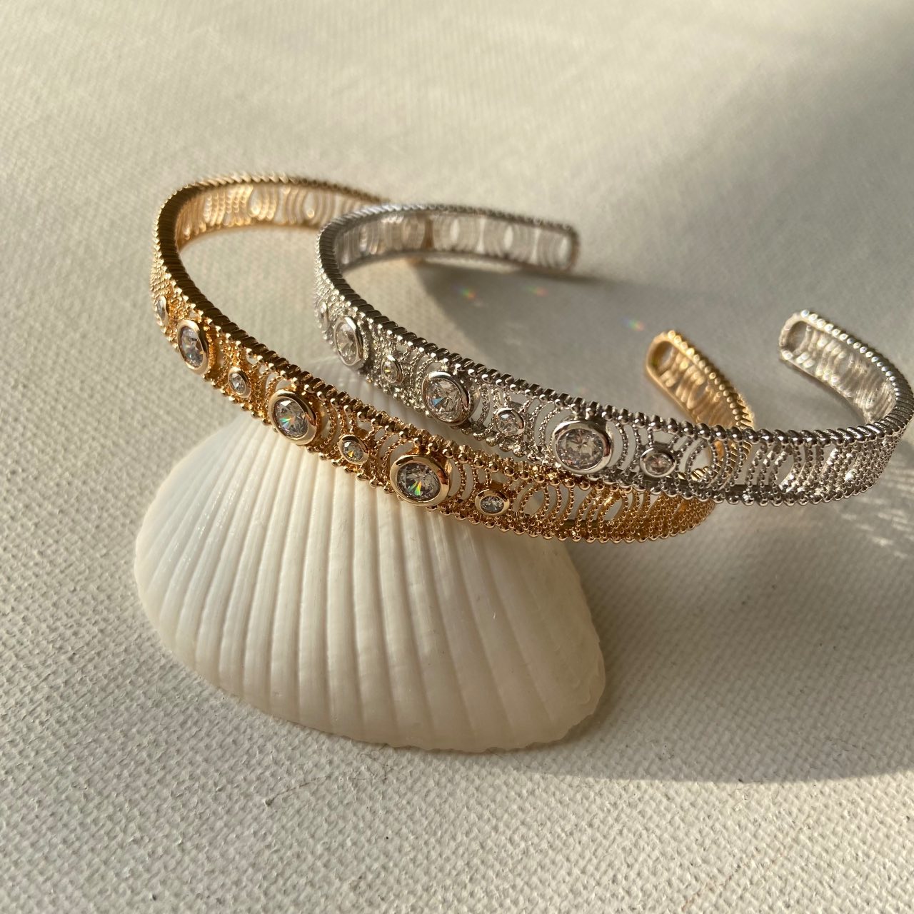 Bracelets ouverts doré et argenté ornés de strass, posés sur un coquillage, bijou chic