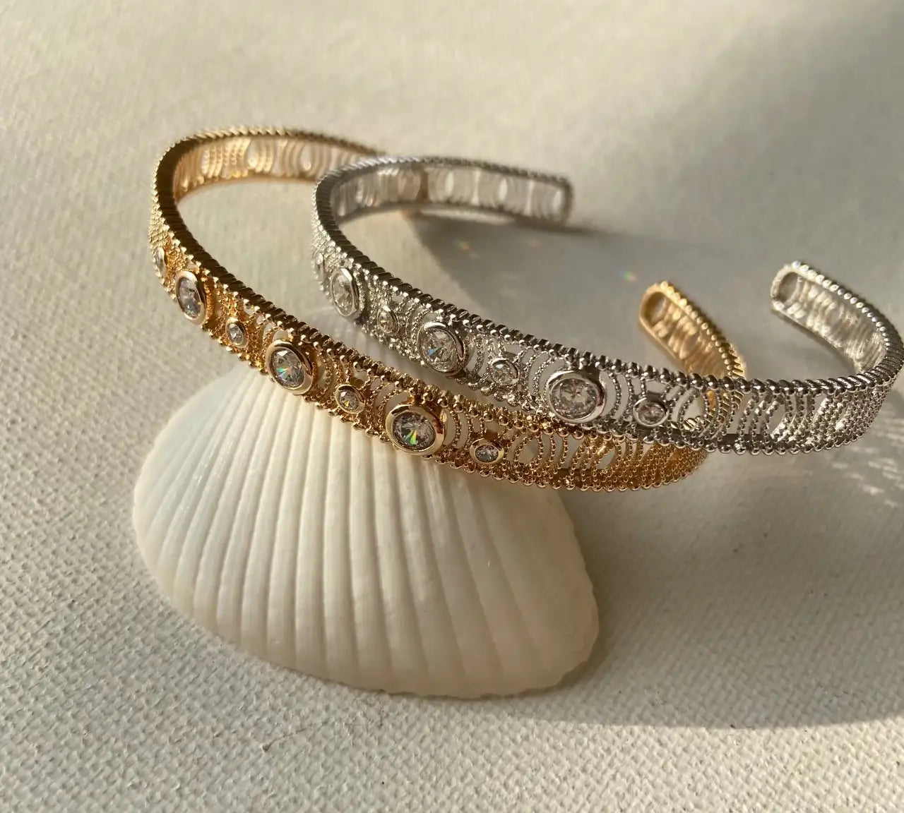 Bracelets ouverts doré et argenté ornés de strass, posés sur un coquillage, bijou chic
