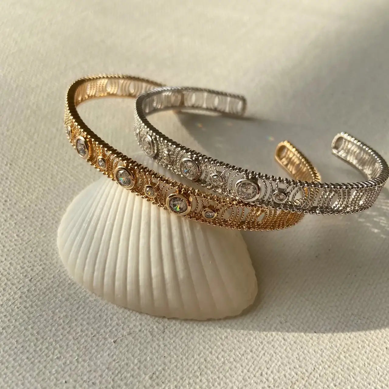 Bracelets ouverts doré et argenté ornés de strass, posés sur un coquillage, bijou chic