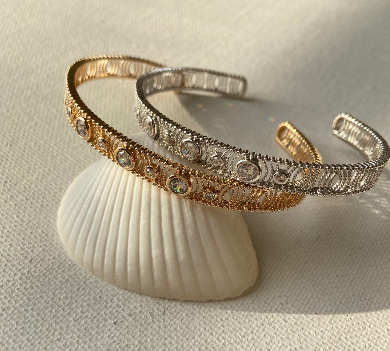 Bracelets ouverts doré et argenté ornés de strass, posés sur un coquillage, bijou chic