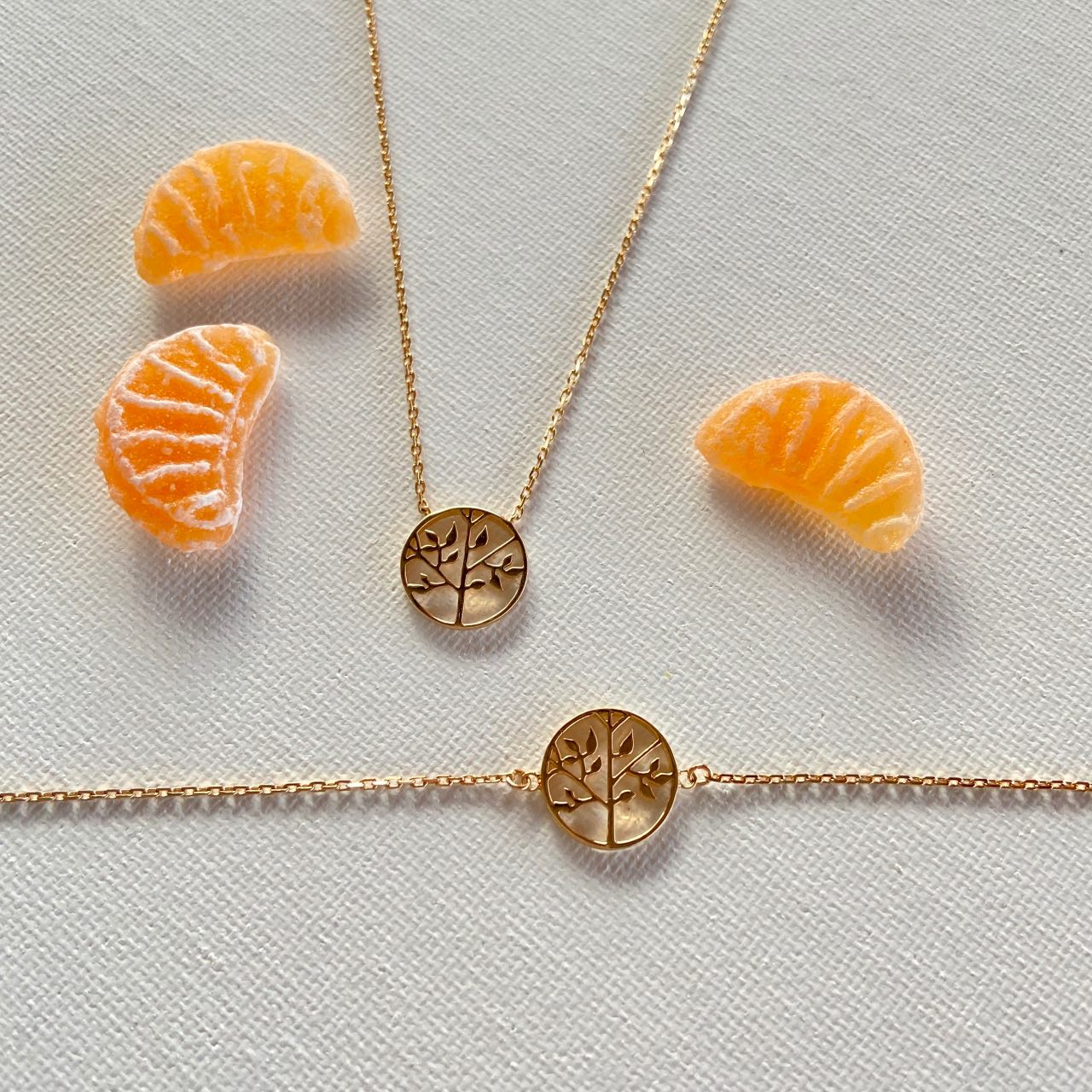 Collier et bracelet dorés arbre de vie sur fond blanc avec quartiers d'orange décoratifs