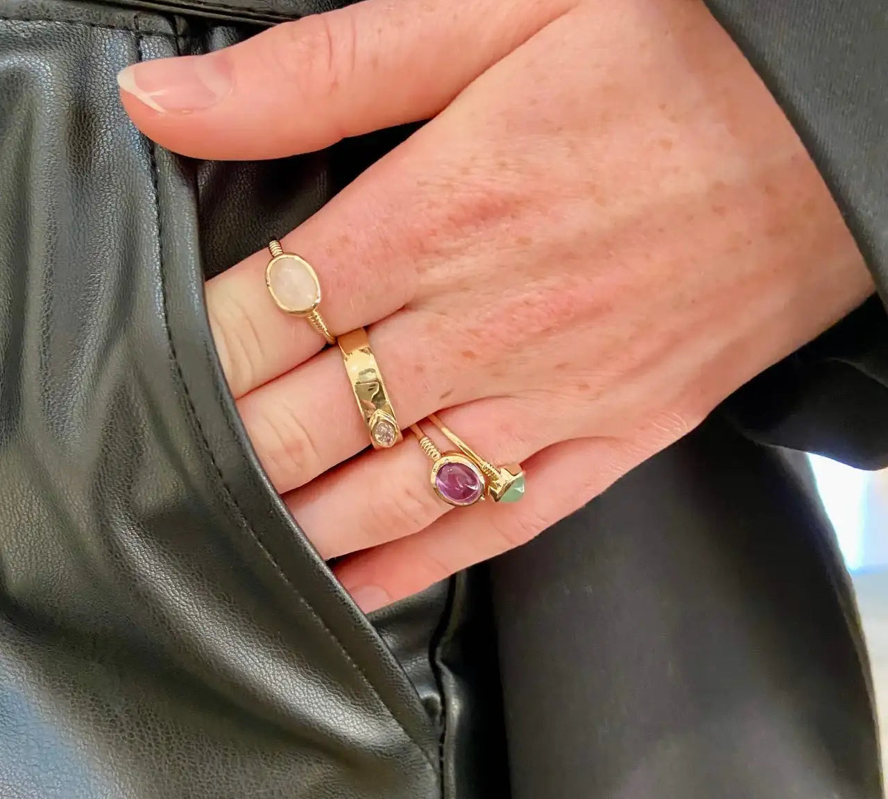 Trois bagues tendance en plaqué or avec pierres colorées portées sur une main.