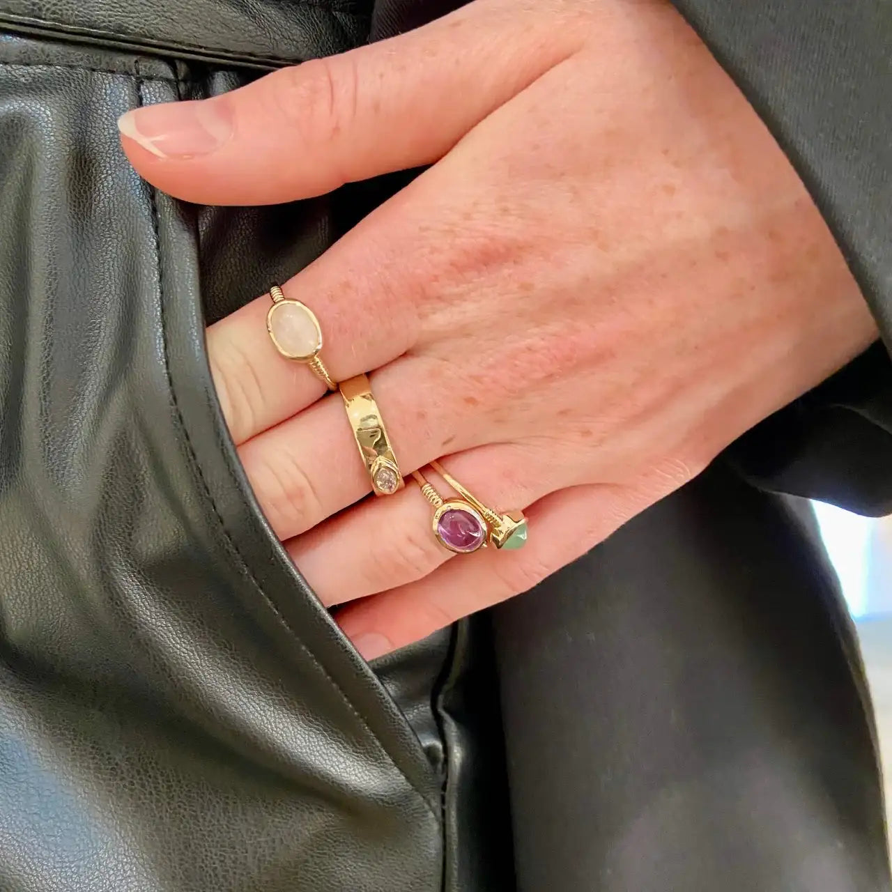Trois bagues tendance en plaqué or avec pierres colorées portées sur une main.