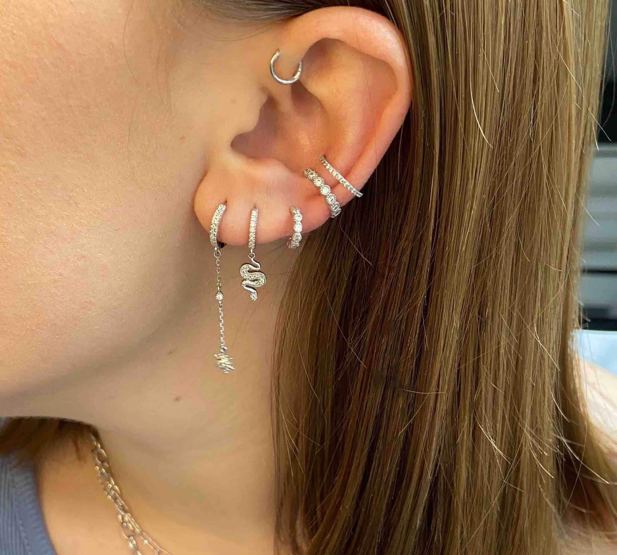 Boucle d’oreille chic en argent serpent et strass portée sur une oreille de femme, style tendance.