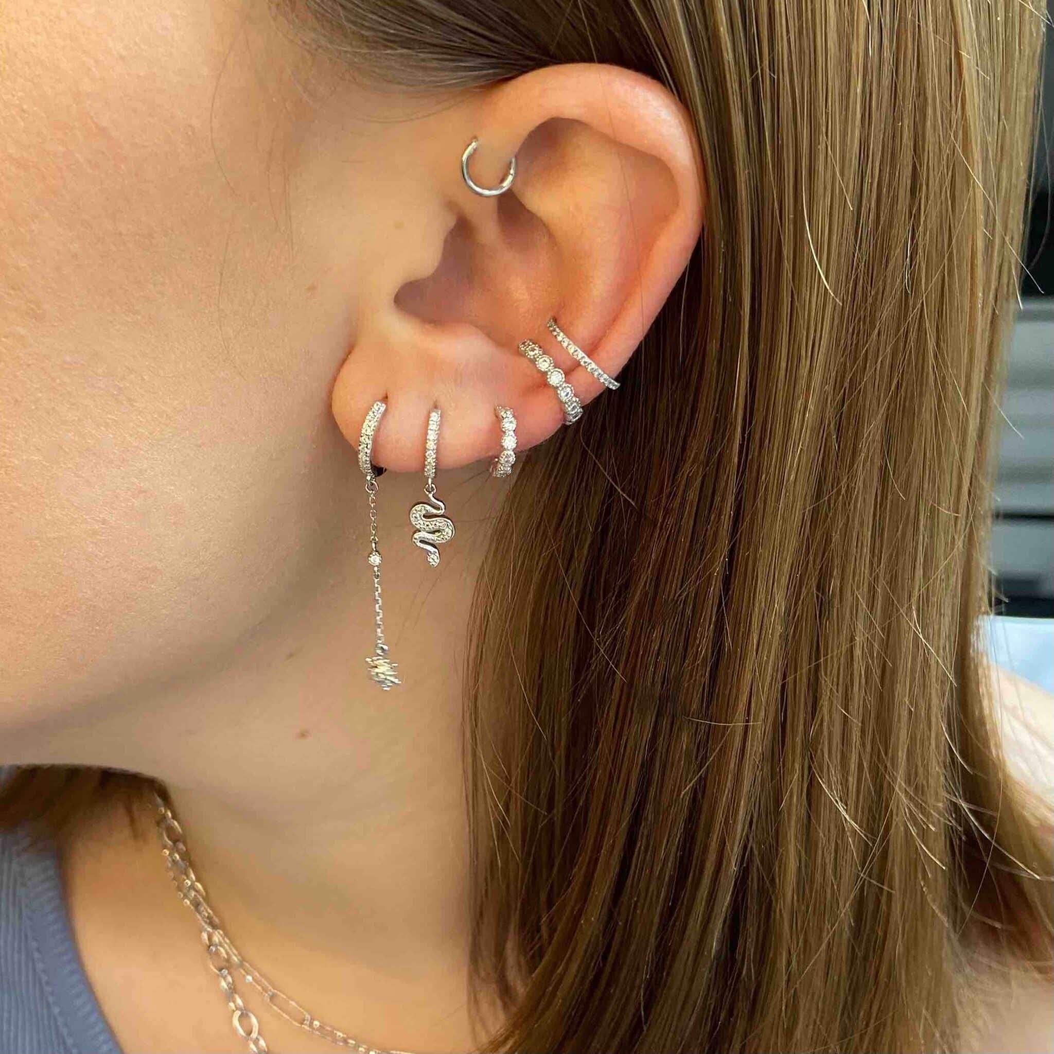 Boucle d’oreille chic en argent serpent et strass portée sur une oreille de femme, style tendance.