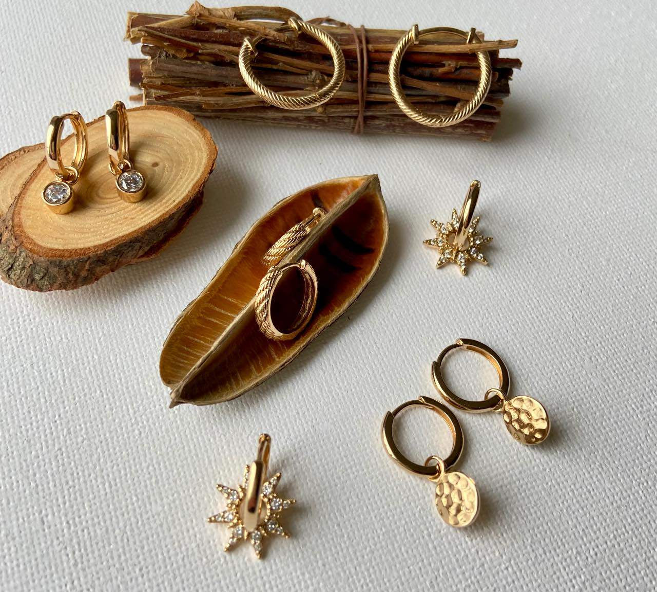 Boucles d’oreilles créoles dorées chic posées sur fond blanc et éléments naturels