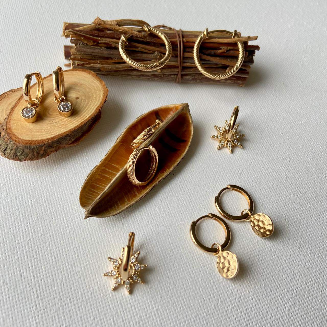 Boucles d’oreilles créoles dorées chic posées sur fond blanc et éléments naturels