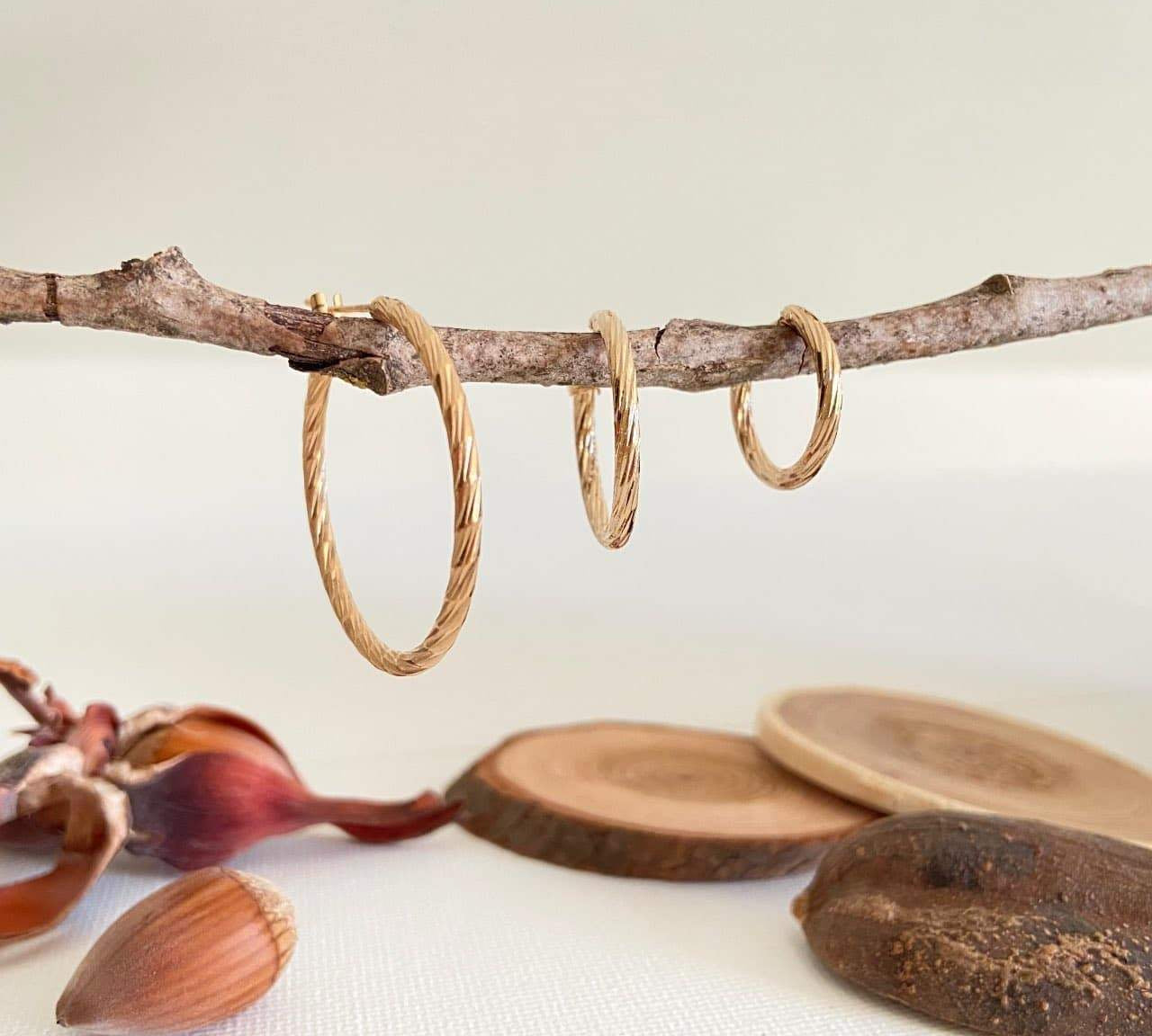 Trois paires de boucles d'oreilles créoles torsadées en plaqué or suspendues à une branche.