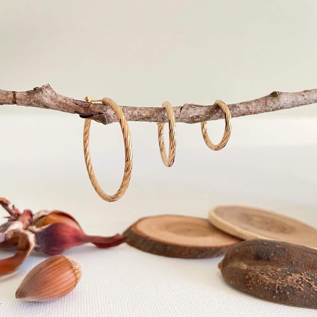 Trois paires de boucles d'oreilles créoles torsadées en plaqué or suspendues à une branche.