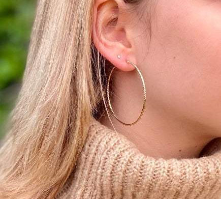 Gros créoles en plaqué or portés par une femme aux cheveux blonds.