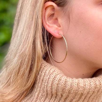 Gros créoles en plaqué or portés par une femme aux cheveux blonds.