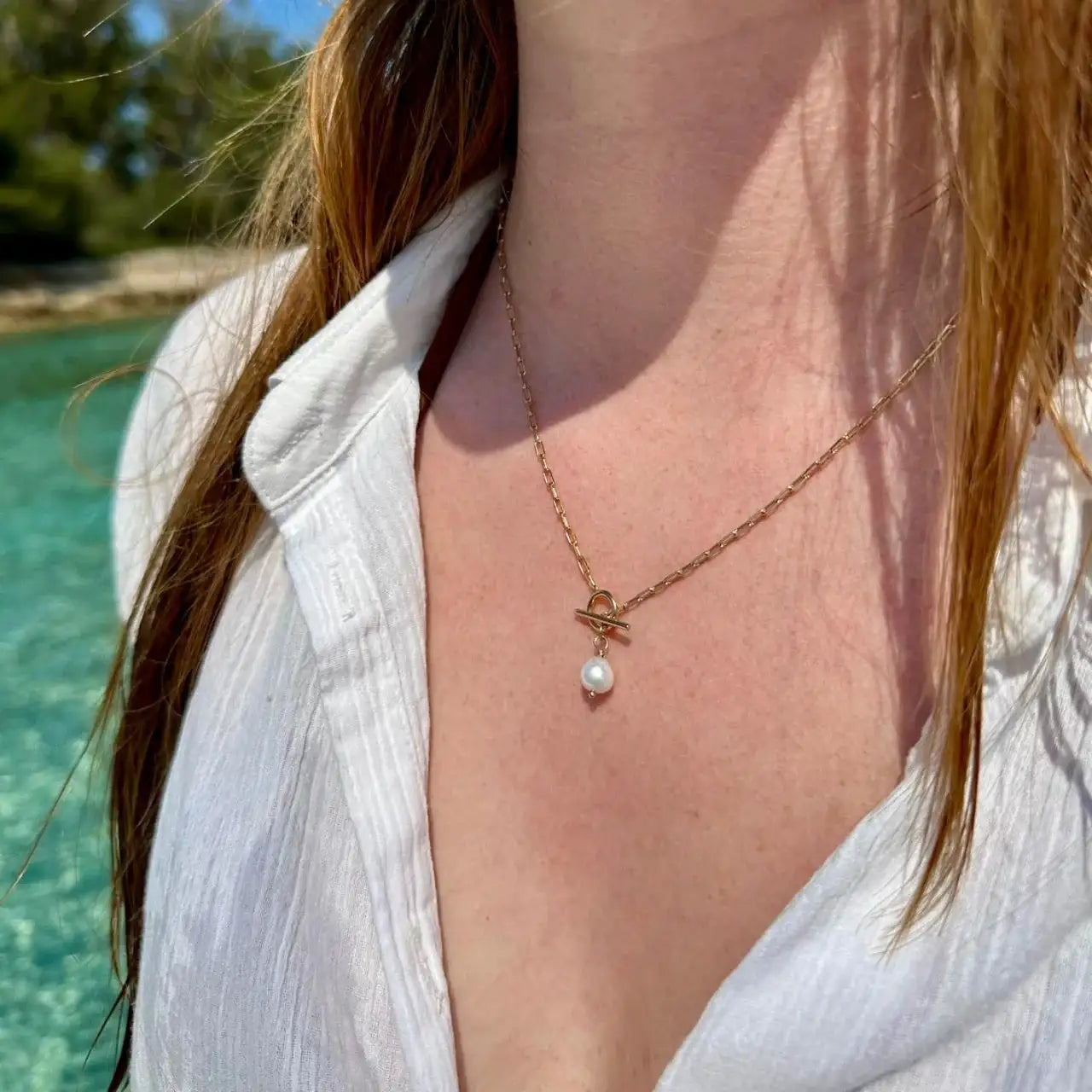 Collier fin en plaqué or avec perle blanche porté par une femme