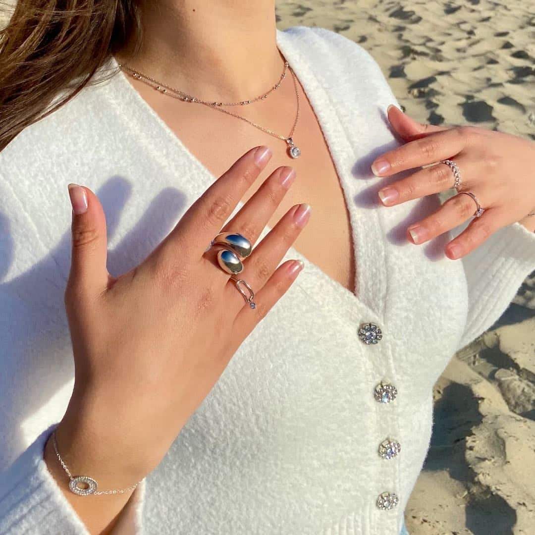 Femme portant une grosse bague argent, colliers et bracelets élégants sur une plage ensoleillée