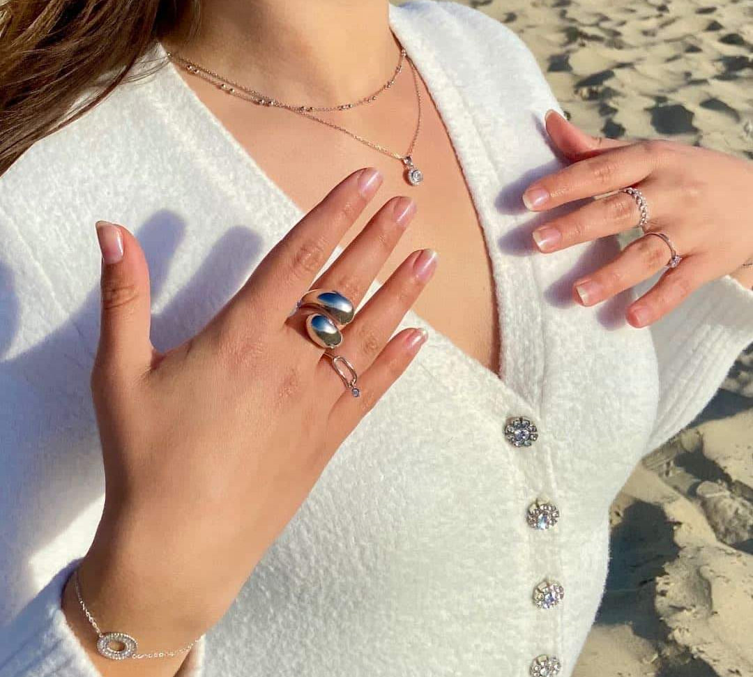 Femme portant une grosse bague argent, colliers et bracelets élégants sur une plage ensoleillée