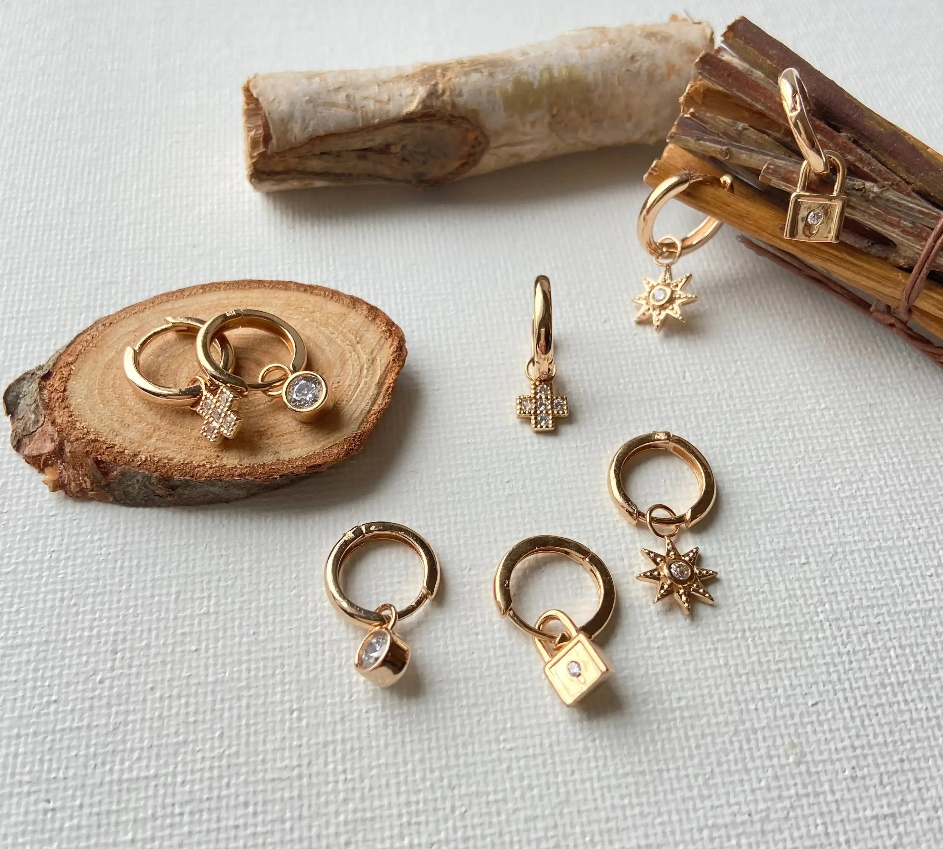 Assortiment de boucles d'oreilles anneaux en plaqué or avec pendentifs variés sur fond blanc.