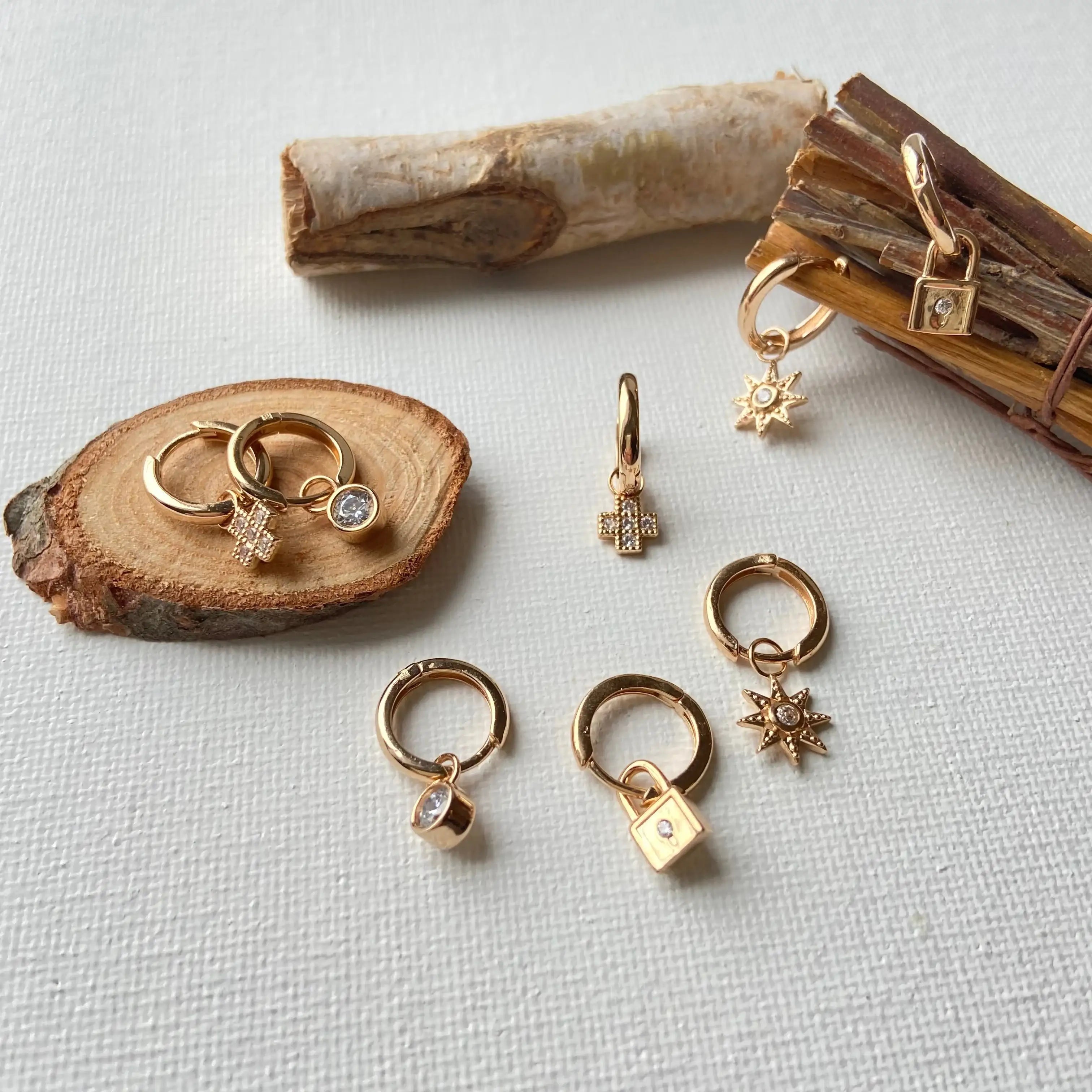Assortiment de boucles d'oreilles anneaux en plaqué or avec pendentifs variés sur fond blanc.