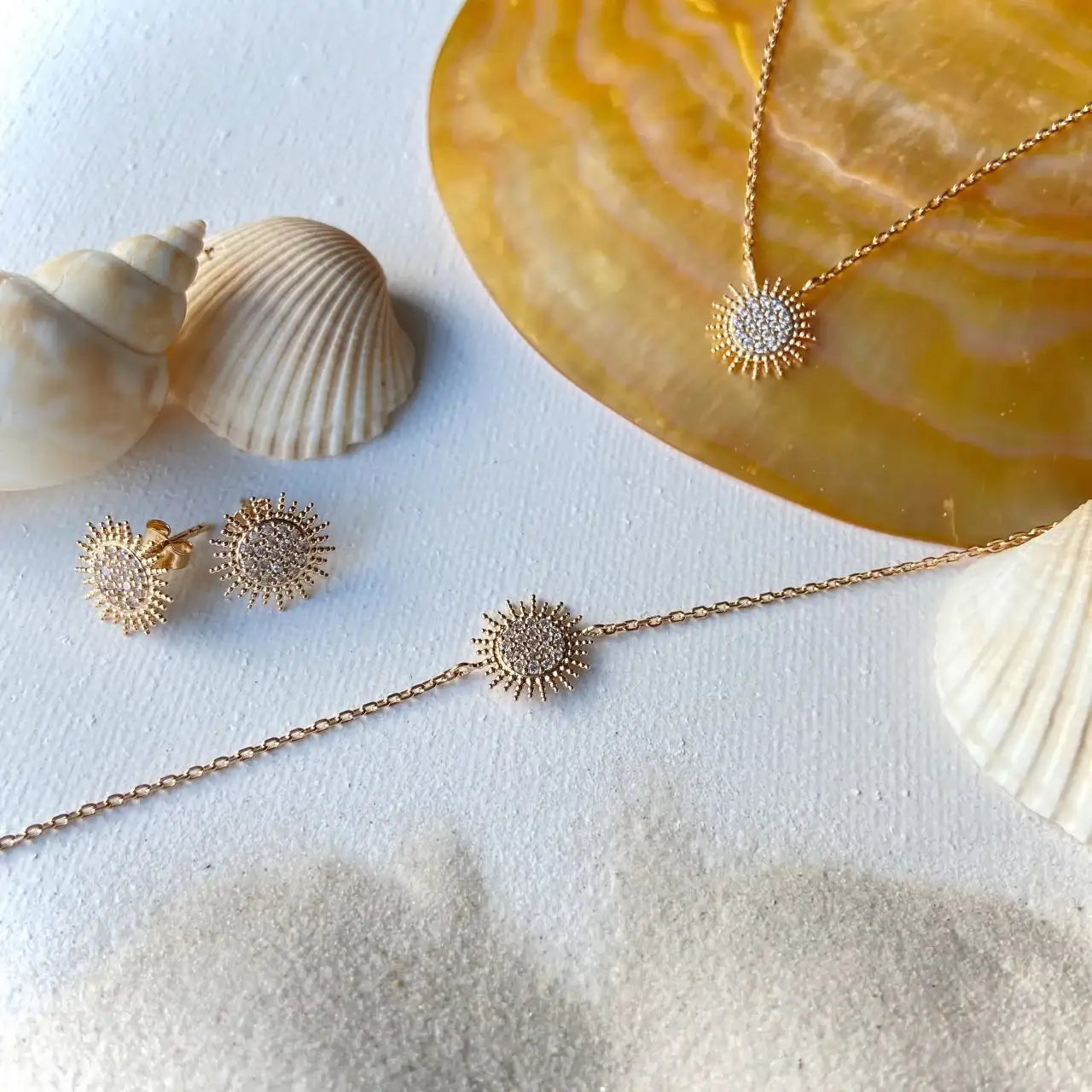 Parure de bijoux plaqués or 18 carats avec motif soleil et diamants sur fond de plage