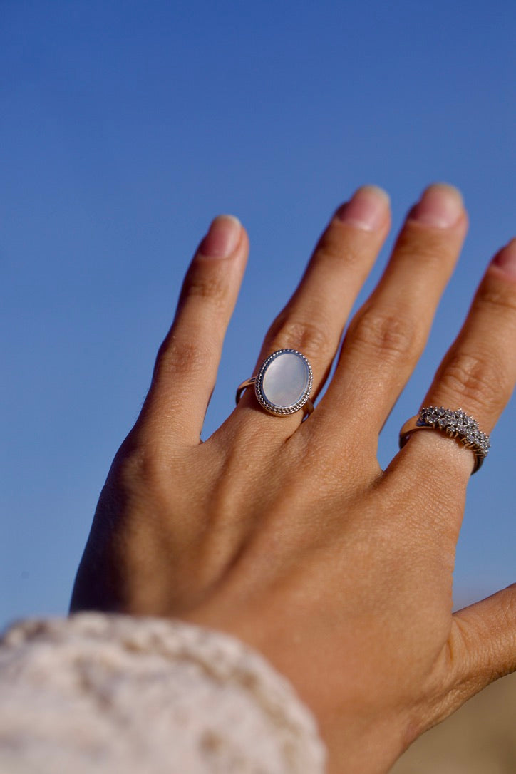 Main posée sur une robe fleurie, portant deux bagues dorées tendance, bijoux chic femme.