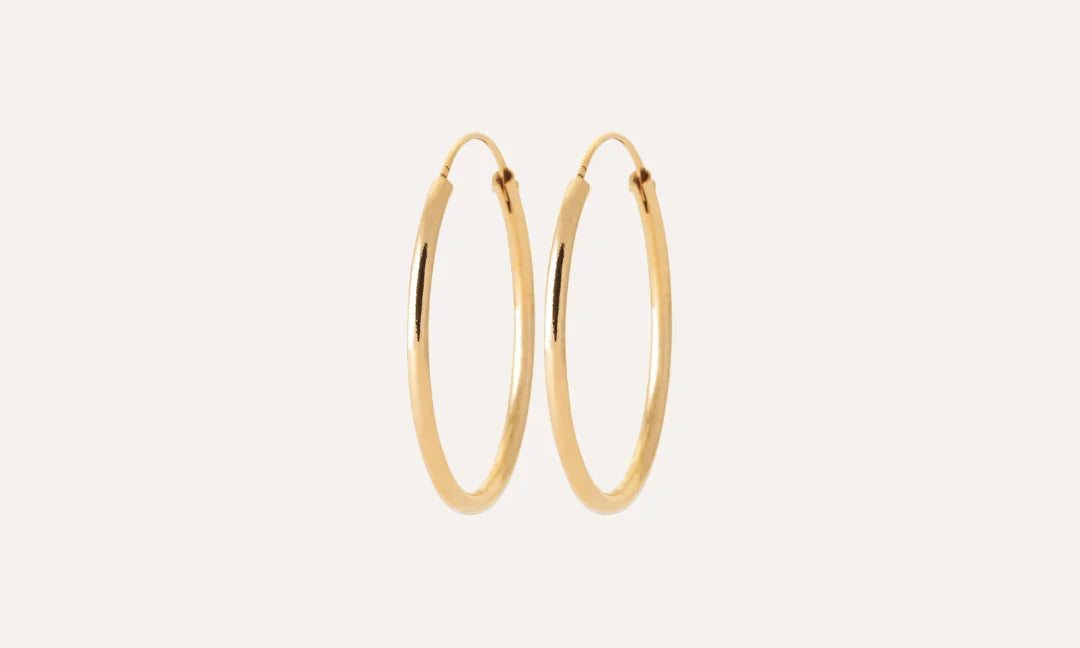 Paire de boucles d’oreilles créoles fines en métal doré sur fond uni, style chic.