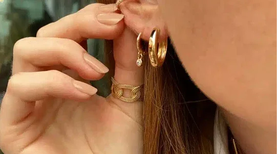 Femme portant créoles dorées, bague et bijoux élégants sur l’oreille et la main