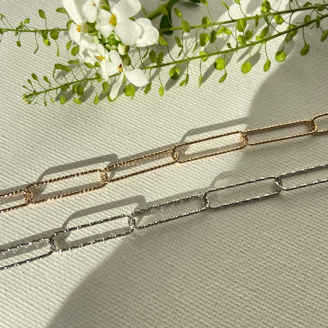 Bracelets chaîne maille rectangulaire doré et argenté sur fond fleuri élégant