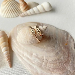 Bague plaqué or avec motif plumes posée sur des coquillages blancs