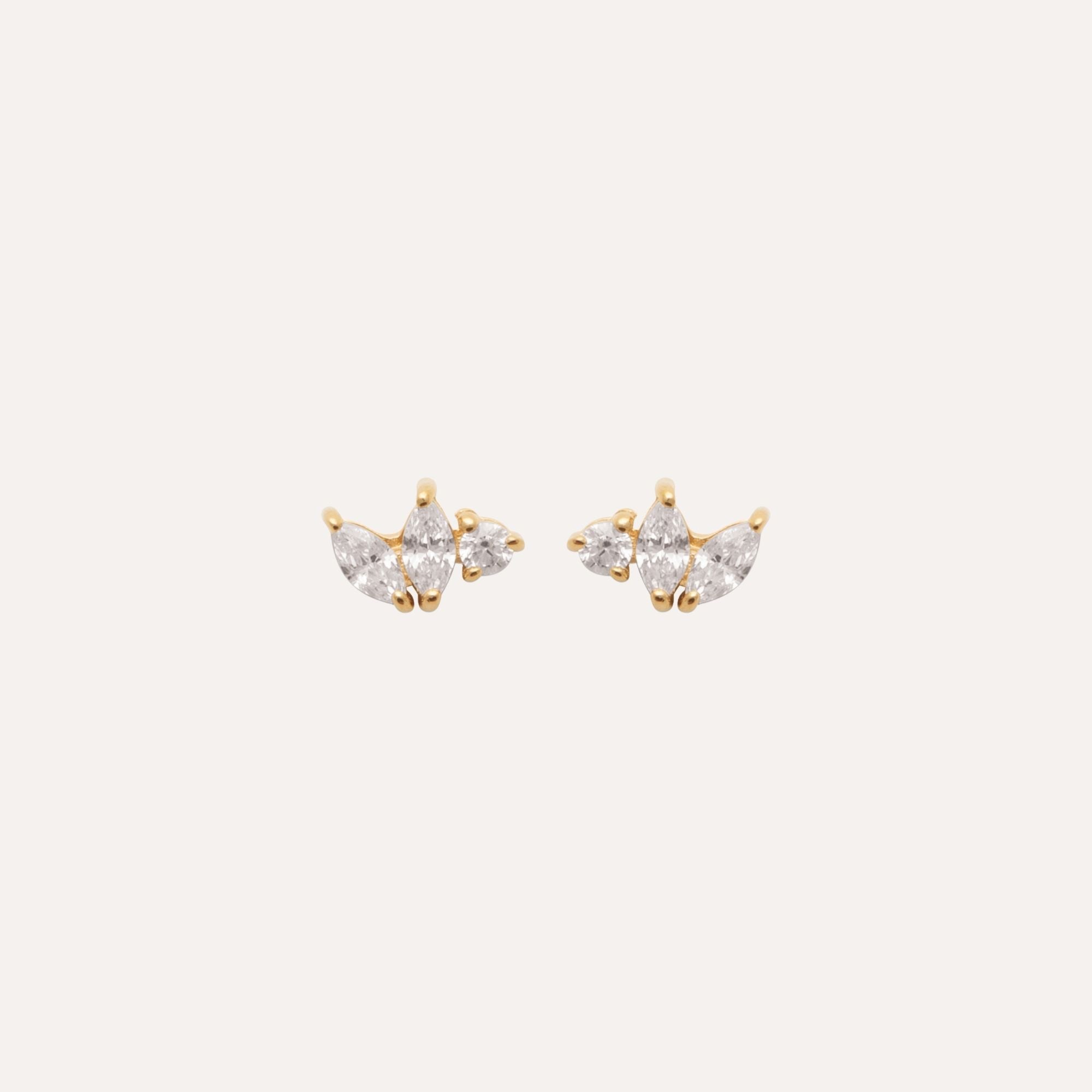 Boucles d’oreilles puces dorées avec trois zircons, style chic et élégant, fond clair.