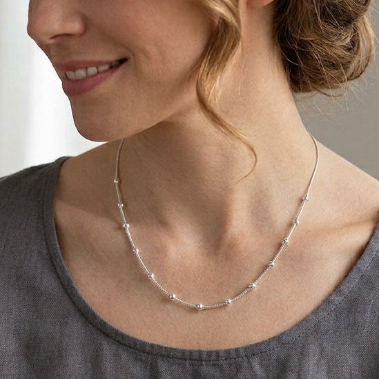 Collier chaine argent boules porté par une femme blonde avec un chemiier gris
