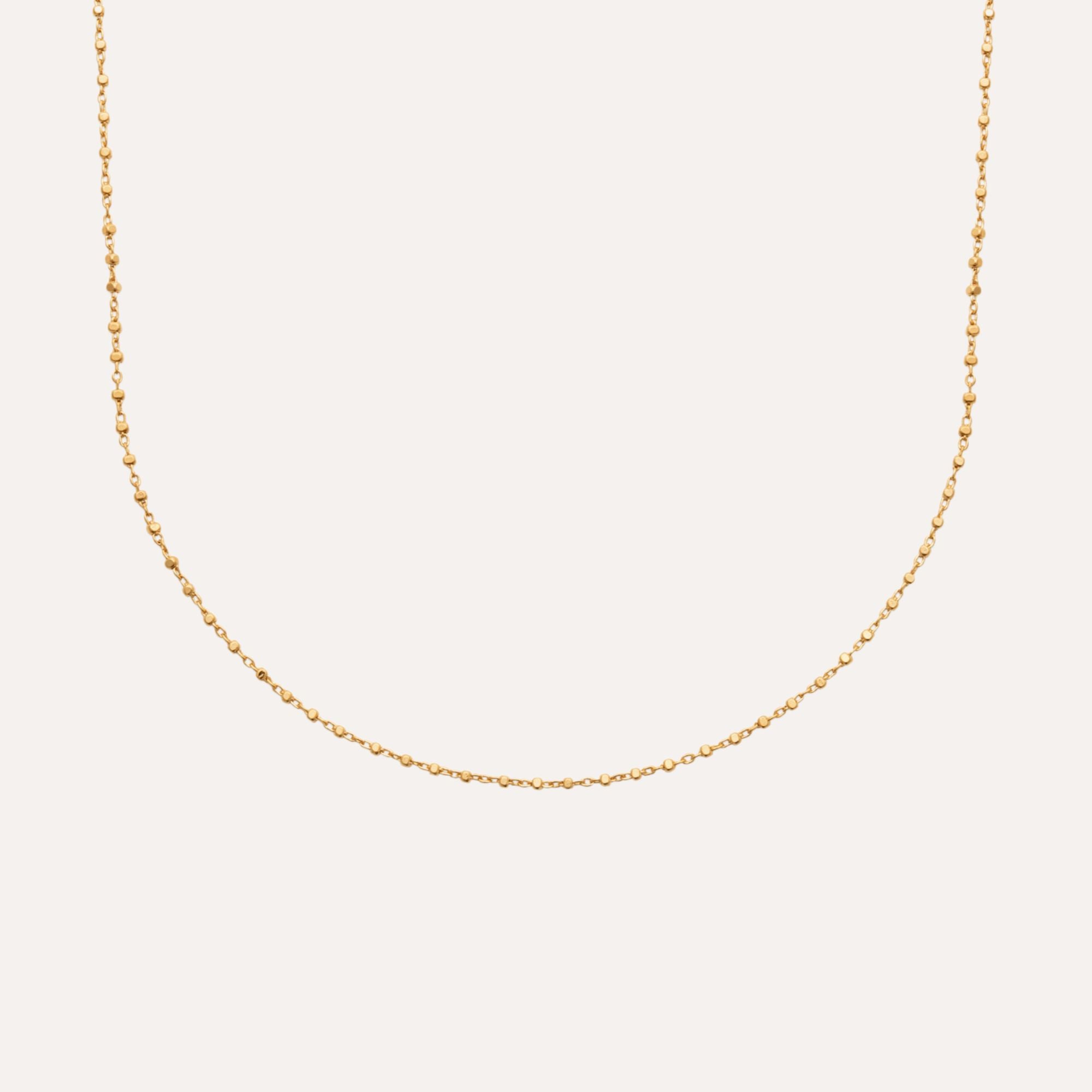 Collier fin doré à petites perles pour femme, bijou chic sur fond blanc.
