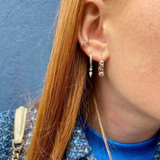 Petites créoles en argent portées par une jeune fille aux cheveux roux sur fond bleu